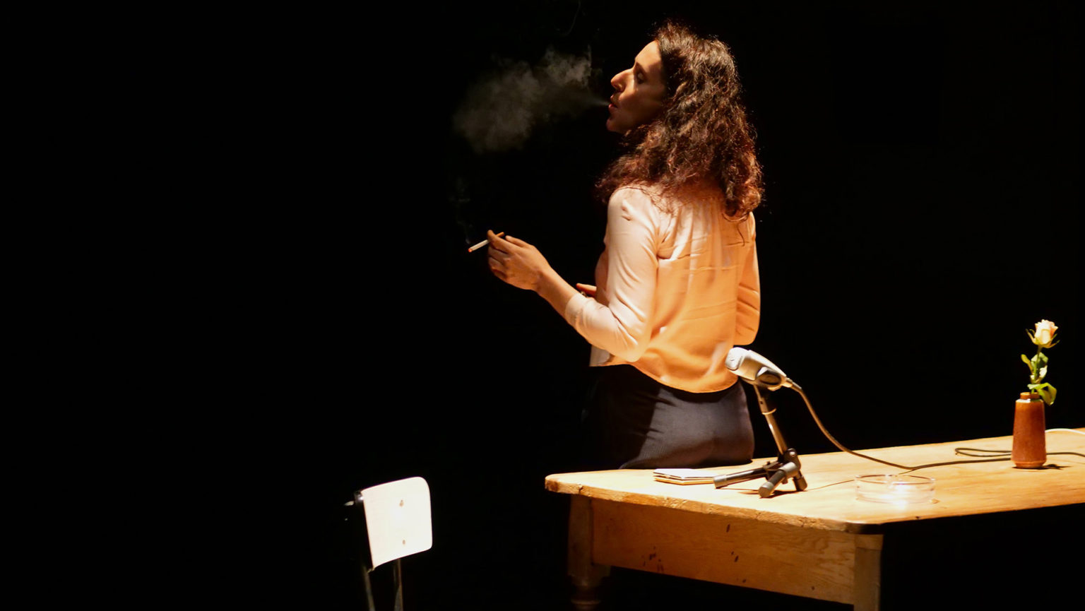 Jasmina Doueib est debout, de dos, la tête légèrement sur le côté, et elle fume une cigarette