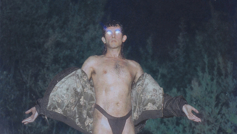 Alberto Cortés pose en sous-vêtement devant un champ à la tombée de la nuit. Il écarte les bars et ses yeux sont rempli d'une lumière blanche qui reflète.
