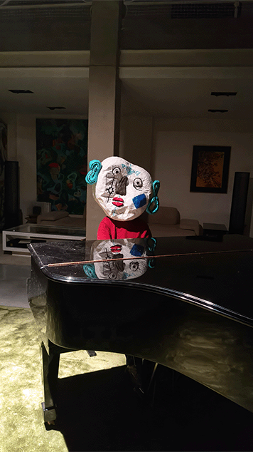Une personne portant un masque coloré et artistiquement déformé est assise derrière un piano au milieu d'une grande pièce.