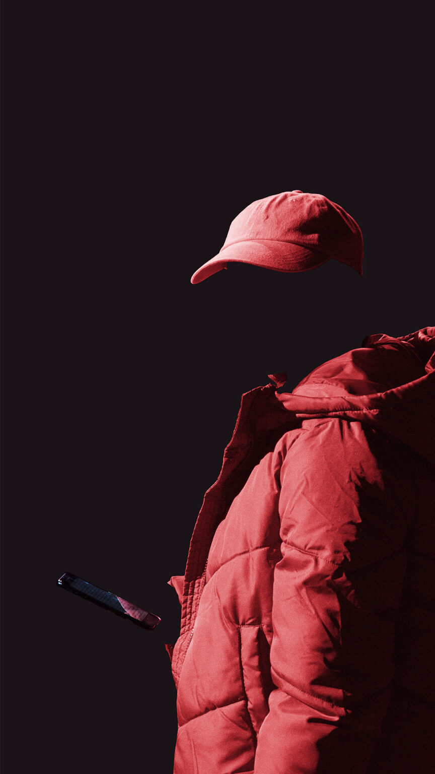 Le visage d'une personne entièrement vêtue de rouge se fond dans le noir de l'arrière plan.